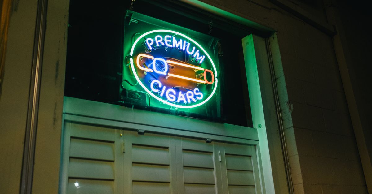 Illuminated neon sign for premium cigars outside a building at night.